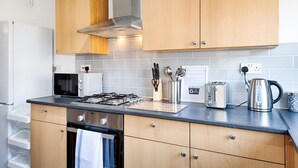 A modern kitchen with wooden cabinets, a gas stove, a toaster, and a kettle. - 4-Bed Swansea City Home | Walk to Centre | Ideal for Groups (Swansea)