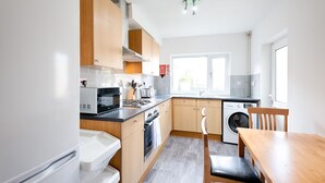 A modern kitchen with wooden cabinets, a microwave, a stove, and a washing machine. - 4-Bed Swansea City Home | Walk to Centre | Ideal for Groups (Swansea)
