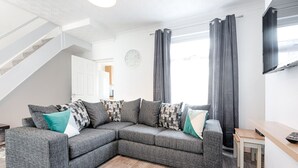 A modern living room with a grey sectional sofa, a wooden coffee table, a staircase, and a flat-screen TV mounted on the wall. - 4-Bed Swansea City Home | Walk to Centre | Ideal for Groups (Swansea)