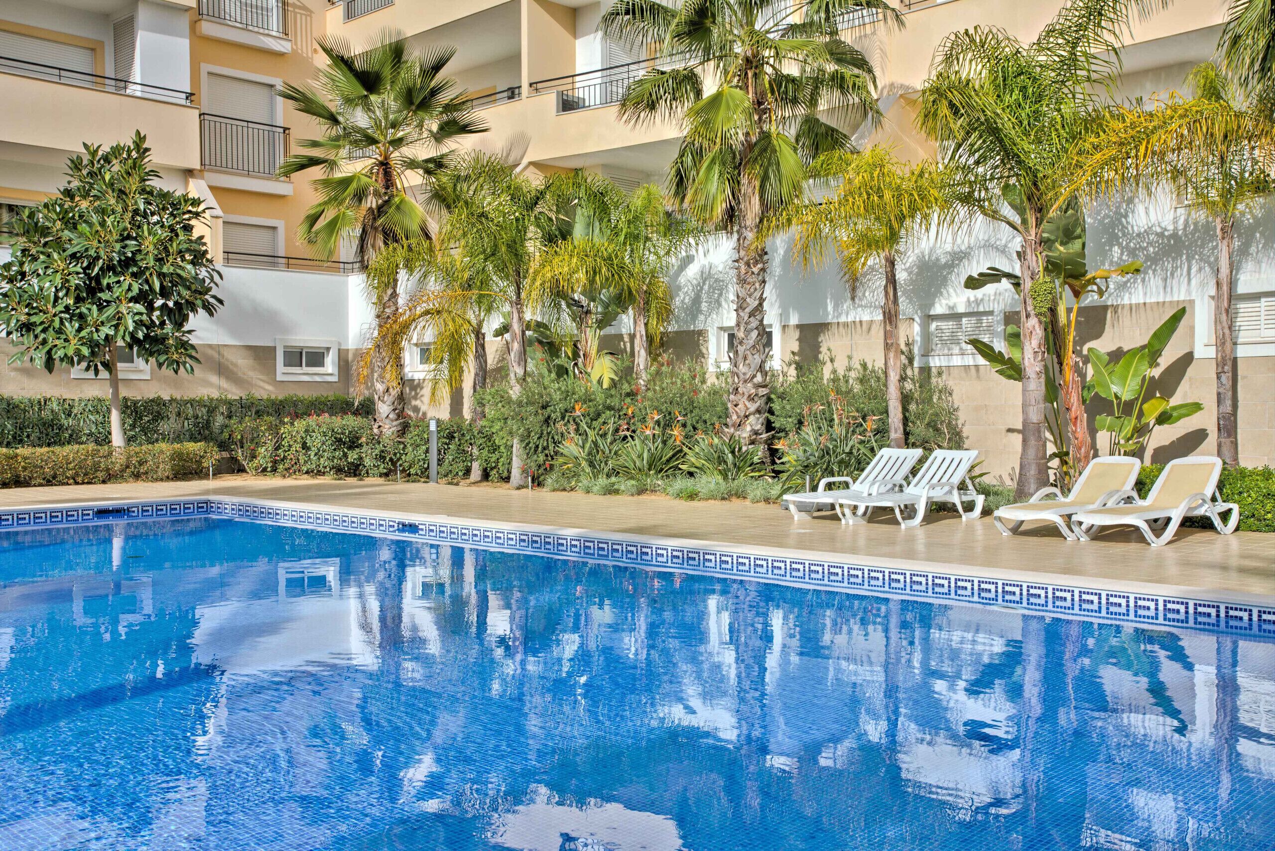 Ein Pool mit Liegestühlen, umgeben von Palmen und einem mehrstöckigen Gebäude.