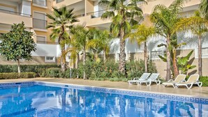Una piscina con sillas de descanso, rodeada de palmeras y un edificio de varios pisos.
