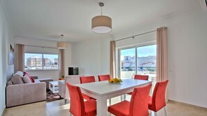 Una sala de estar moderna con una mesa de comedor blanca y sillas rojas, un sofá y un televisor.