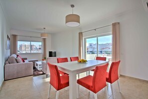 Ein modernes Wohnzimmer mit einem weißen Esstisch und roten Stühlen, einer Couch und einem Fernseher.