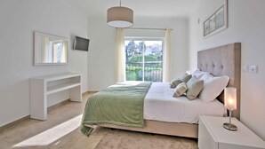 Un dormitorio con cama, televisión, ventana y mesita de noche.