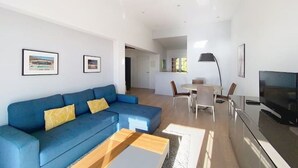 Un soggiorno moderno con un divano blu, un tavolino, una TV e un'area pranzo con sedie e un tavolo.