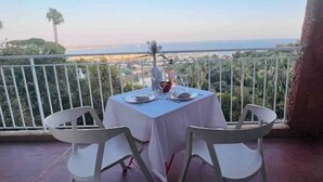 Un tavolo apparecchiato per due su un balcone con vista sul mare e sulla città.