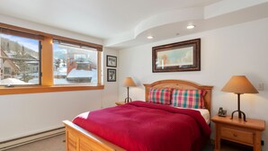 A bedroom with a bed, two bedside tables, a window with a view of a snowy landscape, and a framed picture on the wall. - 4208 - One Bedroom Standard Creekside Condominiums 1 Condo (Solitude)