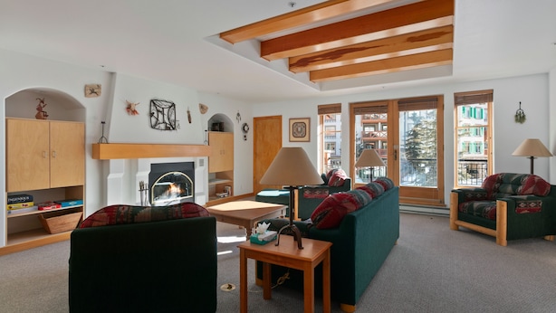 A cozy living room with a sofa, a table, and a lamp. There are wooden beams on the ceiling and a fireplace. - 4208 - One Bedroom Standard Creekside Condominiums 1 Condo (Solitude)