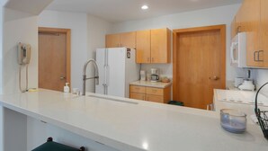 A modern kitchen with white countertops, wooden cabinets, a refrigerator, a coffee maker, and a phone on the wall. - 4208 - One Bedroom Standard Creekside Condominiums 1 Condo (Solitude)