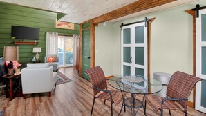 A room with a wooden ceiling, a television mounted on the wall, a dining table with chairs, and a green wall. - Modern Arts District Loft With Boat Parking 1 Bedroom Cottage (Somerset)