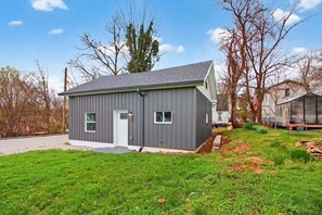 A small, single-story building with a gray exterior, a white door, and two windows. - Modern Arts District Loft With Boat Parking 1 Bedroom Cottage (Somerset)