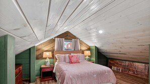 An attic bedroom with a sloped ceiling, a bed with pink bedding, two bedside tables with lamps, and a green wall. - Modern Arts District Loft With Boat Parking 1 Bedroom Cottage (Somerset)
