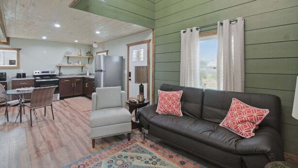A cozy living room with a sofa, chairs, and a rug. There is a kitchen area with cabinets and appliances. - Modern Arts District Loft With Boat Parking 1 Bedroom Cottage (Somerset)