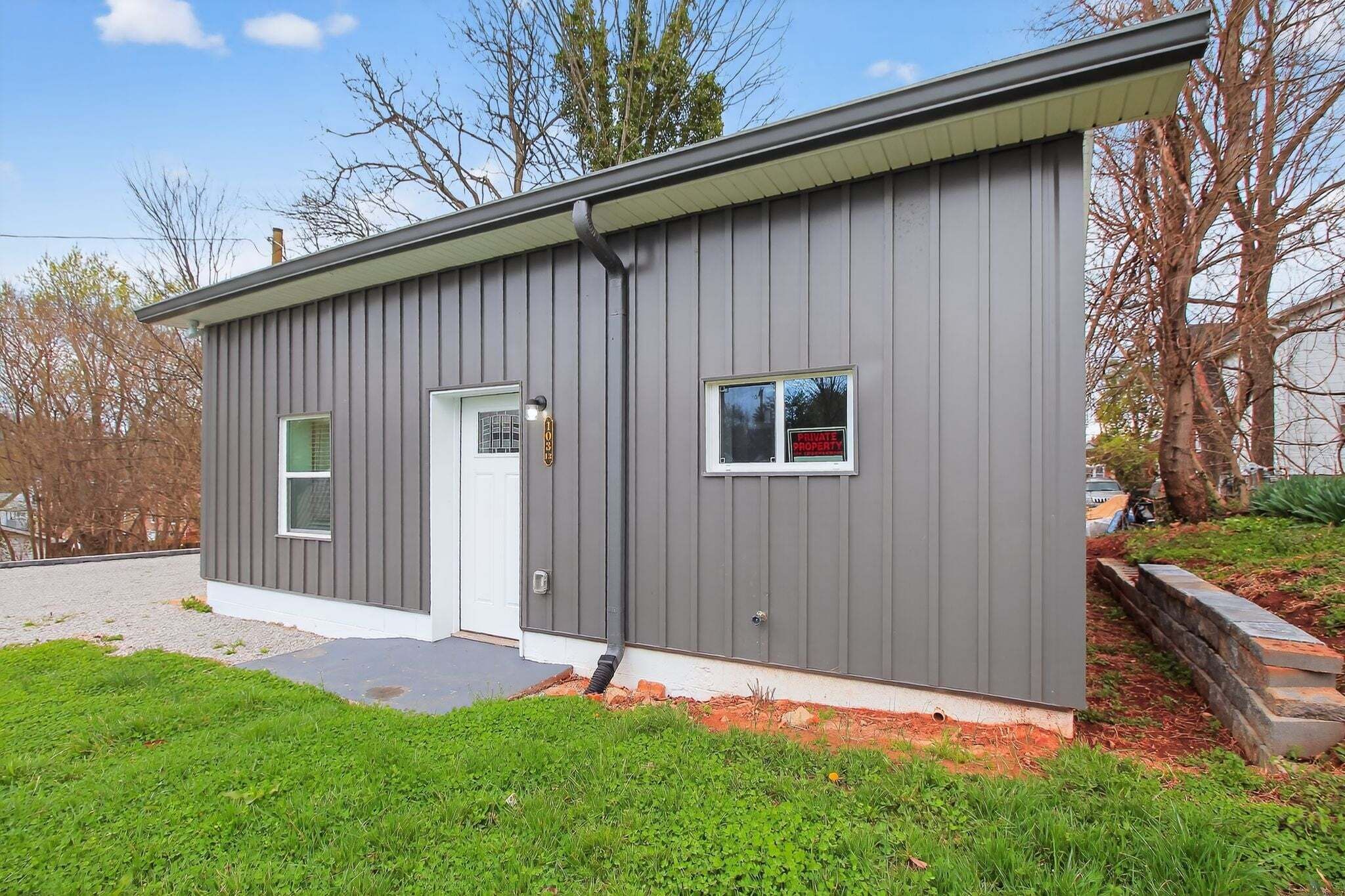 A modern single-story building with a grey exterior, a white door, and a small window.