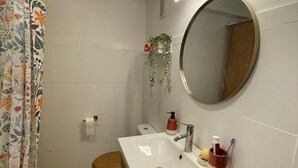 Kylpyhuone, jossa on valkoinen pesuallas, peili, wc-istuin ja suihkuverho.