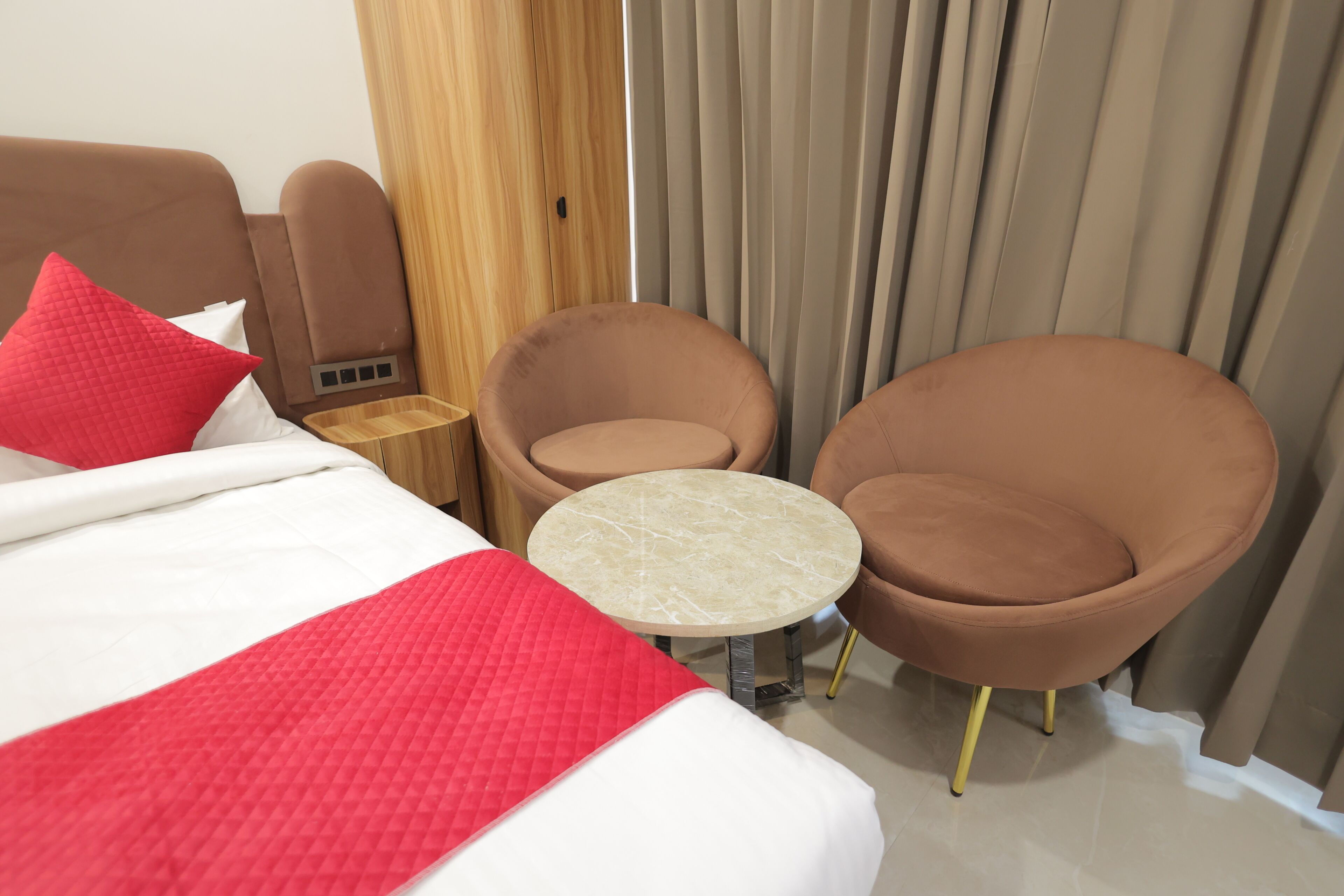 Een hotelkamer met een bed, twee stoelen, een tafeltje en een houten garderobe.
