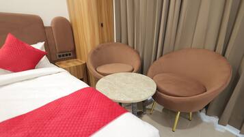 Een hotelkamer met een bed, twee stoelen, een tafeltje en een houten garderobe.