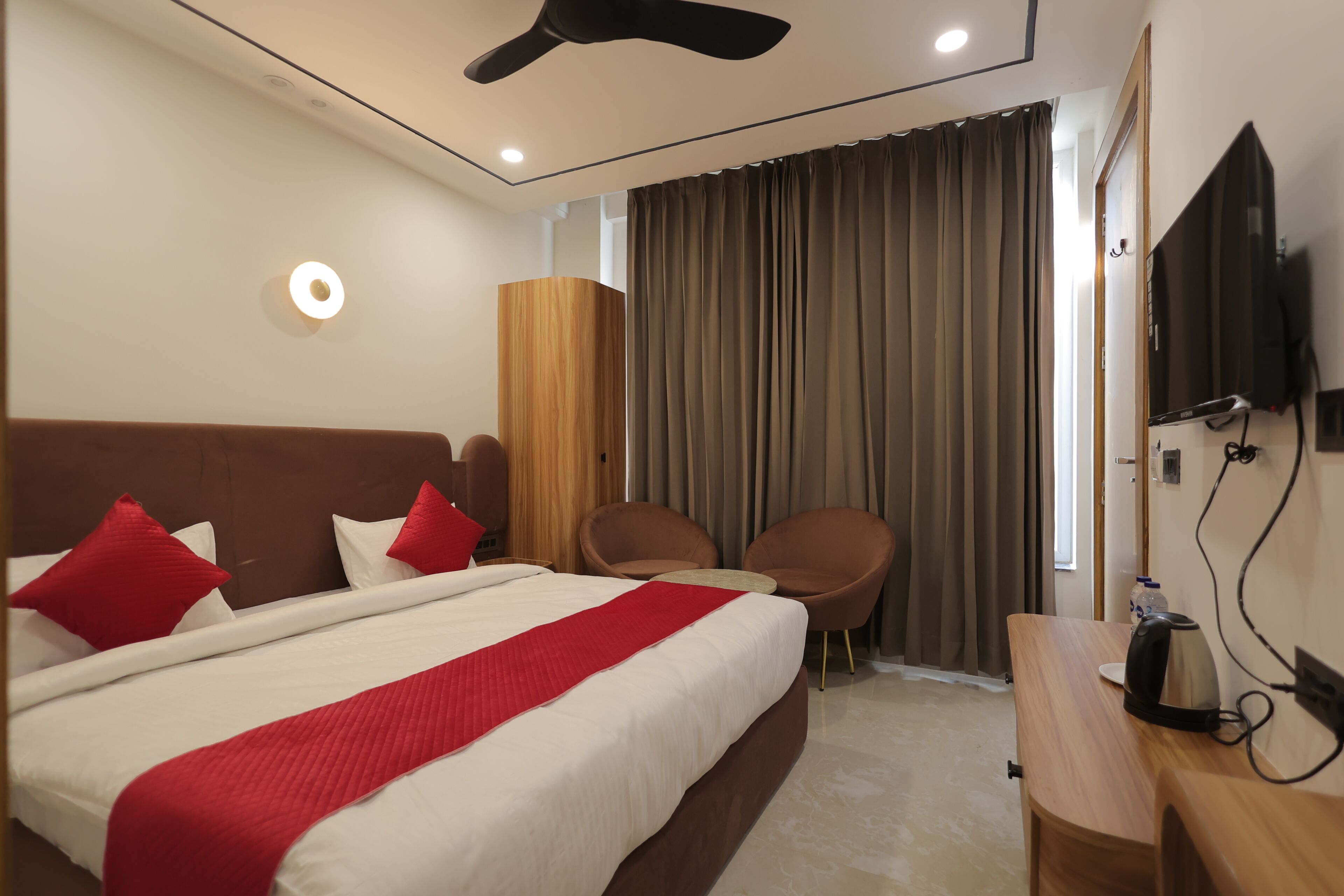 A hotel room with a bed, two chairs, a TV, and a wooden desk.