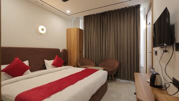 A hotel room with a bed, two chairs, a TV, and a wooden desk.