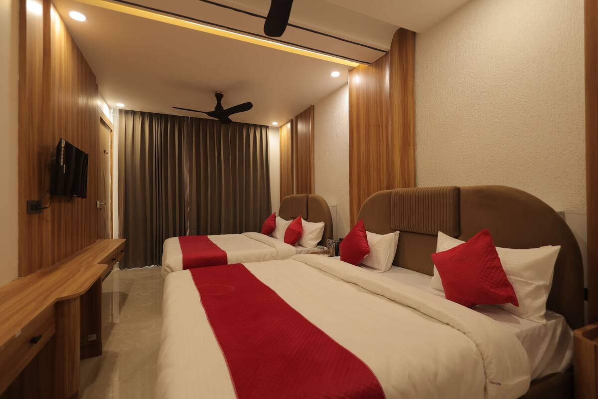 A hotel room with two beds, a wooden desk, a ceiling fan, and a TV on the wall.