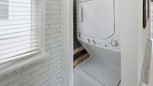 A laundry room with a white brick wall, a window with blinds, and a stacked washer and dryer. - Pet Friendly Parks & Trails Pleasantville Home (Pleasantville)