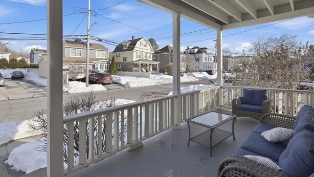 A covered porch with a view of a residential street, a wicker sofa, and a small table. - Pet Friendly Parks & Trails Pleasantville Home (Pleasantville)