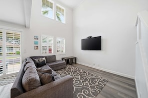 Uma sala de estar moderna com um sofá seccional, uma televisão de tela plana, um tapete estampado e uma janela com persianas.