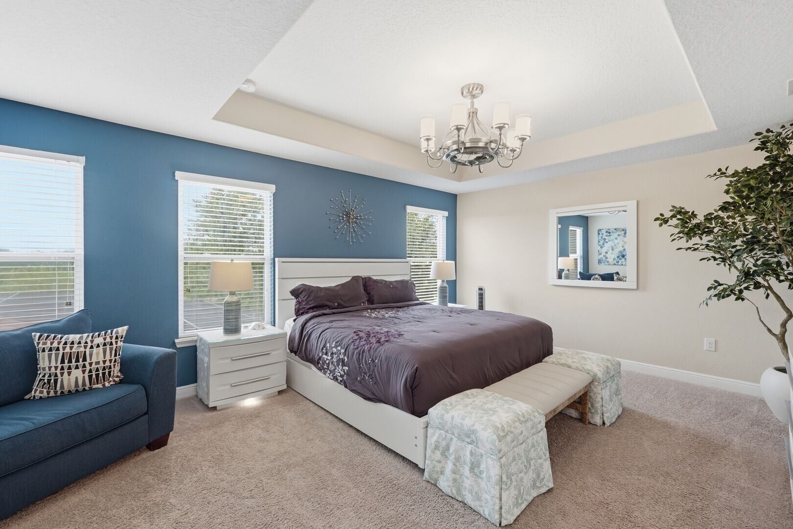 A bedroom with a bed, bedside tables, a bench, a chandelier, and a large window.