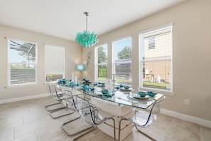 A dining area with a glass table, clear chairs, and a teal chandelier. - St4119ot Solterra Resort 6 Bedroom Home (Davenport)
