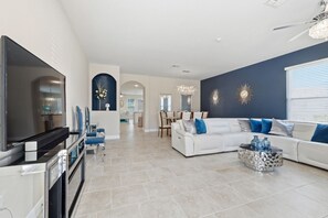 Ein modernes Wohnzimmer mit Flachbildfernseher, einem weißen Sofa und einem Essbereich mit einer Chandelieber.