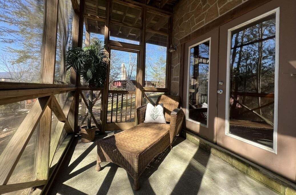 A covered porch with wicker furniture and a potted plant.