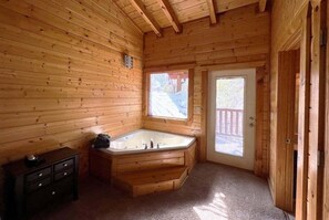 A wooden cabin with a corner bathtub, a small dresser, and a door leading outside. - Airport Runway 33 3 Bedroom Cabin (Pigeon Forge)