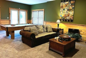 A pool table, a striped sofa, a wooden coffee table, and a wall with a collage of pictures. - Airport Runway 33 3 Bedroom Cabin (Pigeon Forge)