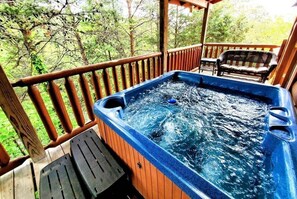 A hot tub on a wooden deck with a bench and a table, surrounded by trees. - Airport Runway 33 3 Bedroom Cabin (Pigeon Forge)