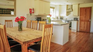 A modern kitchen with wooden cabinetry, a central island, and a dining area with a wooden table and chairs. - Maple Lodge (Knighton)