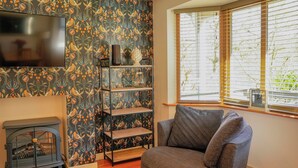 A living room with a fireplace, a television, a sofa, and a window with blinds. - Maple Lodge (Knighton)