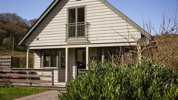 A single-story house with a balcony, a front porch, and a wooden fence. - Maple Lodge (Knighton)