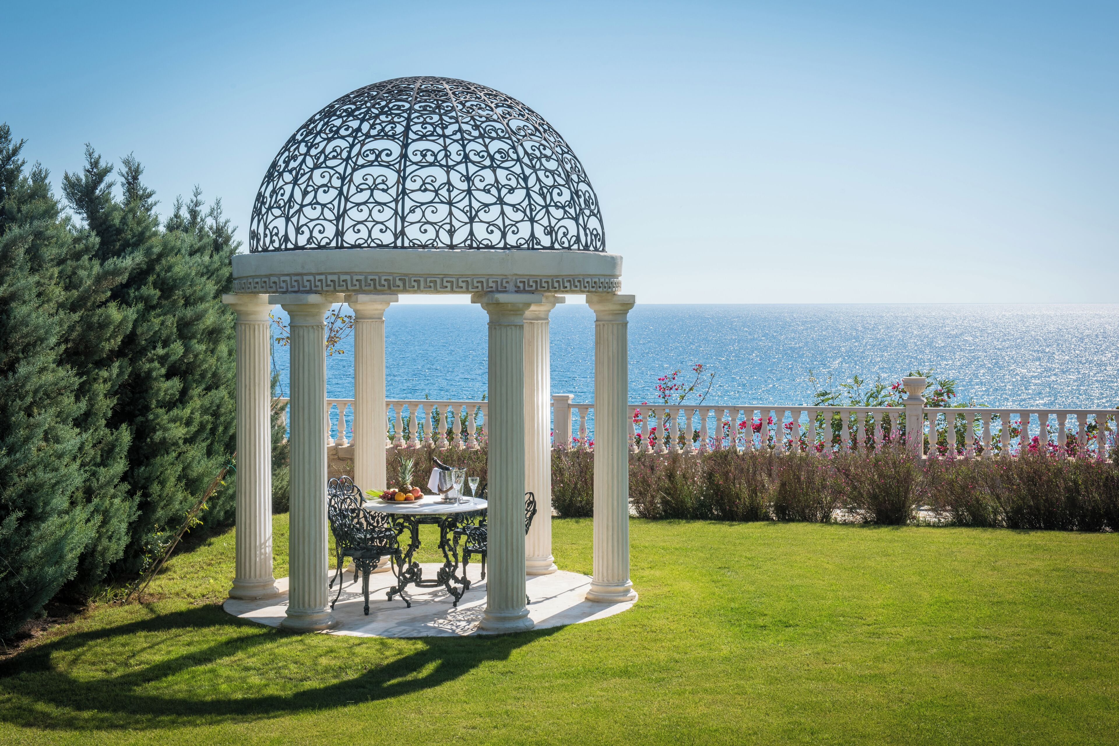 A gazebo with a dome roof, white columns, and a table with chairs.