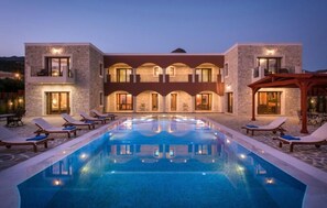 A hotel with a swimming pool, lounge chairs, and a stone facade. - Villa Kastello Kalliste (Ferma)