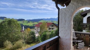A balcony with a view of a rural landscape, including houses and mountains.