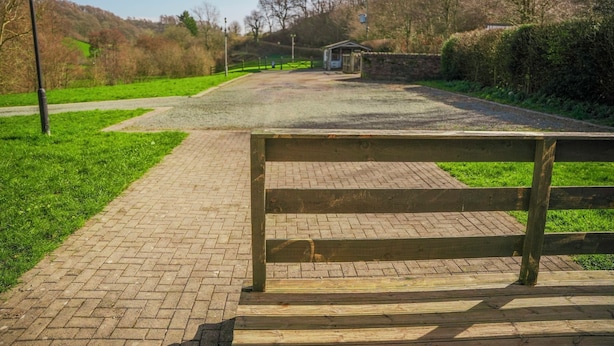 Een geplaveid pad dat leidt naar een klein gebouw, omringd door groen en een glooiend landschap.