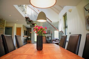 A dining table with chairs, a vase with flowers, a staircase, and a ceiling light fixture. - Oak Lodge (Knighton)
