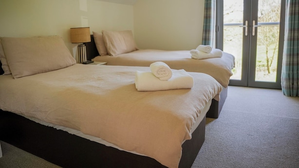 Two beds with beige bedding and towels, a lamp, and a view through a glass door. - Oak Lodge (Knighton)