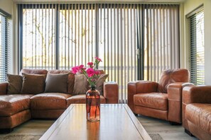 A living room with a brown leather sofa, a wooden coffee table, and a vase with pink flowers. - Oak Lodge (Knighton)