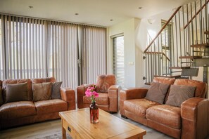 A living room with a brown leather sofa set, a wooden coffee table with a vase of flowers, and a staircase with wooden railings. - Oak Lodge (Knighton)