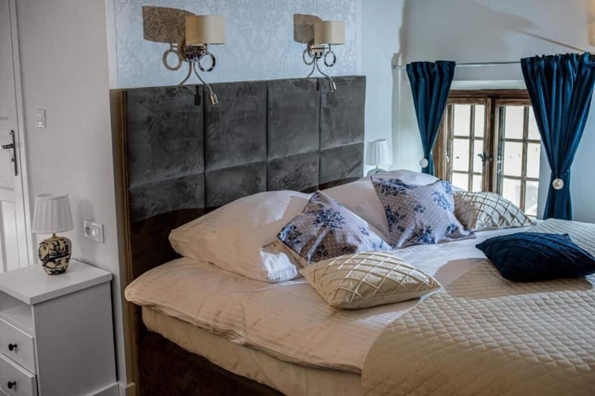Un dormitorio con una cama grande, una mesita de noche, dos lámparas de pared y una ventana con cortinas.