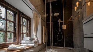 Un baño moderno con cabina de ducha de vidrio, una ventana con cortinas y suelo de mármol.