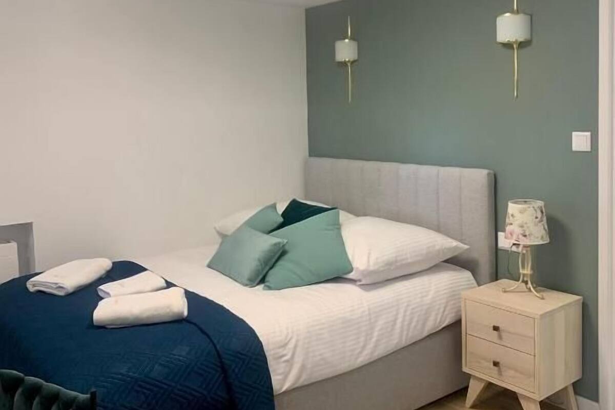 Un dormitorio ordenado con una cama, mesitas de noche y una lámpara.