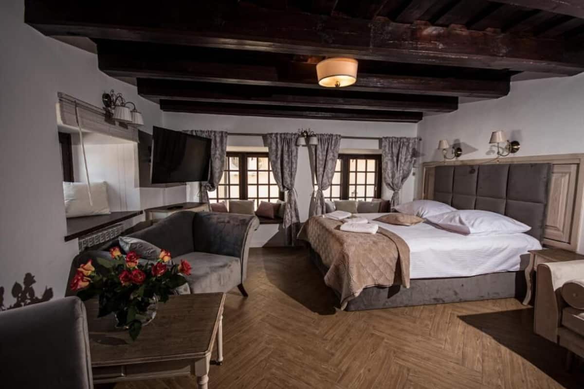 Un dormitorio con cama, una silla, televisor, escritorio y ventana con cortinas.
