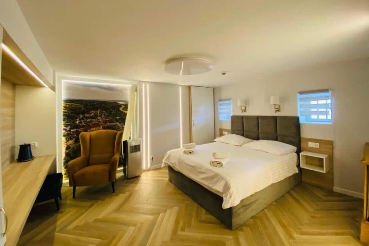 Un dormitorio moderno con una cama, una silla, un televisor montado en la pared y una ventana.